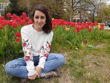 Giuliana Bucci-Mansilla is sitting down on the grass wearing jeans and a white long-sleeve t-shirt. Behind her there are red tulips.